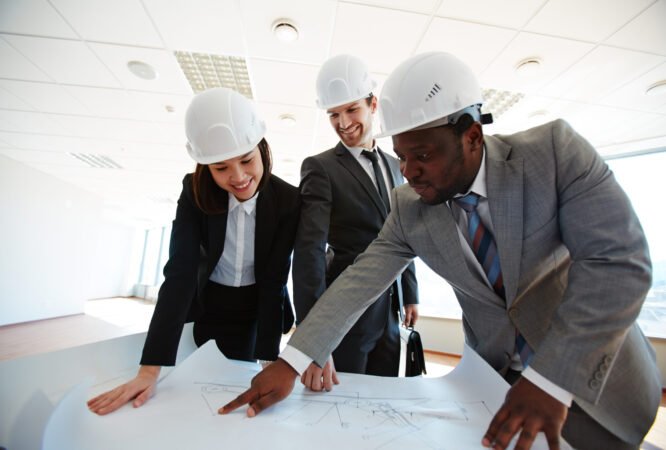 Confident architects in protective helmets looking at blueprint